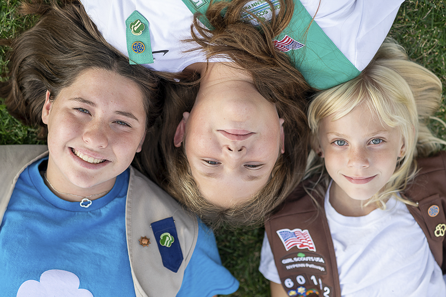 three Girl Scouts of all ages in their vests and smiling at the camera