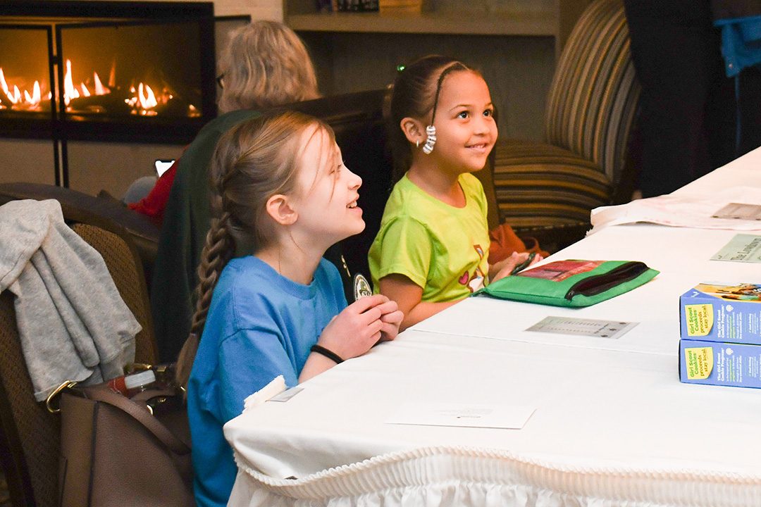 two elementary school girl scouts sitting at a cookie booth
